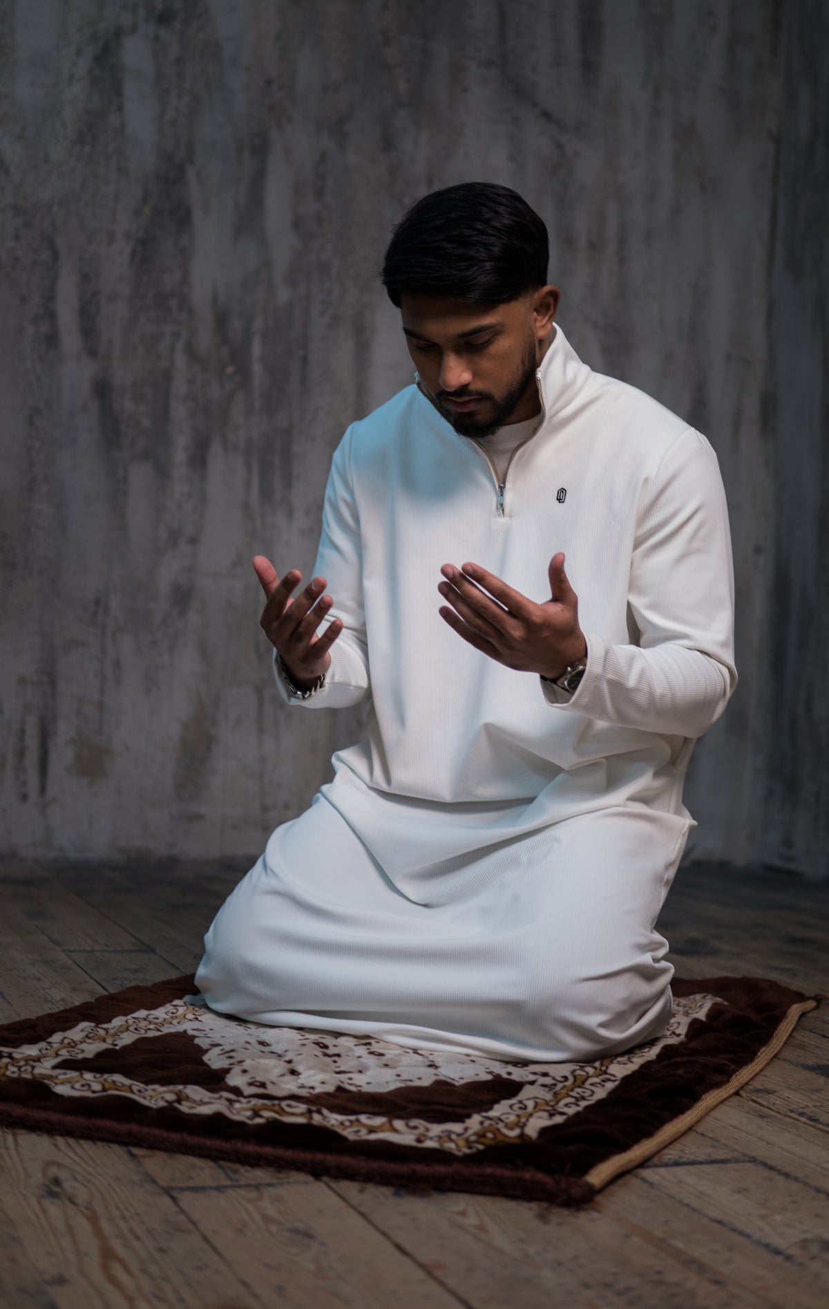 Man in a white Sujud Collection quarter zip thobe praying on a prayer mat